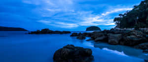 多雲天空下，黃昏時分平靜藍色海水中的深色岩石