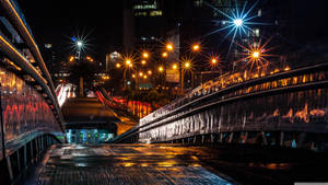夜晚濕潤的城市橋樑，發光的街燈和汽車燈光條紋。 — 3840x2160 壁紙