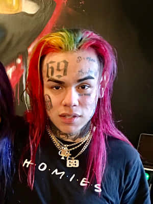 擁有彩色頭髮和面部紋身的人穿著黑色 homies 襯衫。