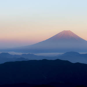 黎明時分的富士山，層疊山巒輪廓上方的粉紅色和藍色天空。