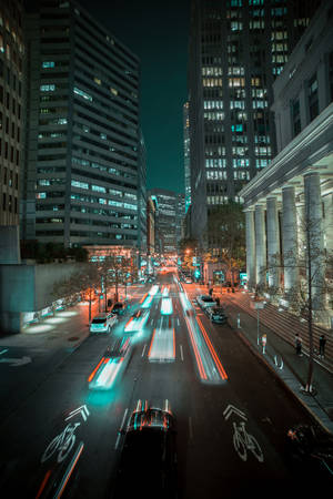 夜間城市街道，高樓之間有移動汽車的燈光軌跡。
