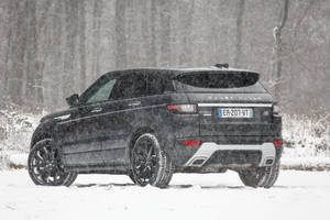 黑色 Range Rover Evoque 在冬季暴風雪中行駛於積雪森林。