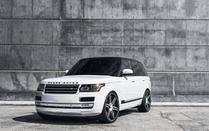 白色Range Rover SUV配備定制輪圈，停靠在混凝土牆前。