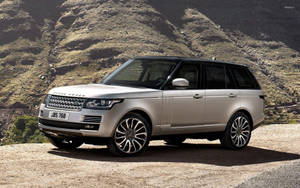 銀色Range Rover SUV停在山路上，後面有山丘。