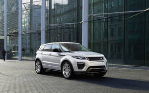 銀色 Range Rover Evoque 停泊在玻璃建築前，附近有行人走過。
