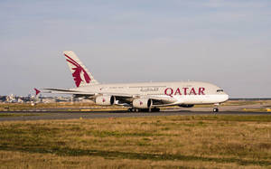 卡塔爾航空A380飛機在機場跑道上，背景有草和城市。