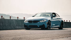 藍色BMW M4轎跑車停泊在沿海道路上，遠處有山丘。