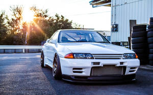 白色日產Skyline R32在日落時停放在輪胎堆附近。