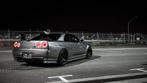 銀色日產GT-R在夜間停放在空地上，帶有發光的紅色尾燈。