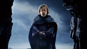 Luke Skywalker 身穿深色斗篷站在岩石懸崖之間，背景是風暴天空