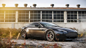 啞黑色Aston Martin停泊在舊工業建築前，夕陽時分。