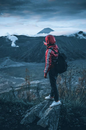 穿著紅色外套的徒步旅行者在黃昏時分俯瞰霧氣瀰漫的火山地形。