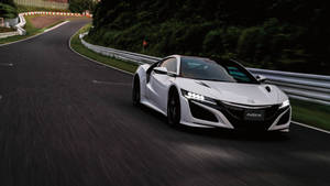 白色Acura NSX在綠樹環繞的彎路上飛馳。