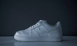 一隻白色Nike Air Force 1波鞋放在灰色表面上，背景深色。 — 型格 Nike 壁紙