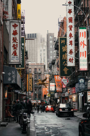 繁忙的唐人街街道，有中文招牌和行人走在灰濛濛的天空下。