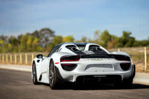 白色保時捷918 Spyder跑車在陽光普照的道路上，背景有樹木。