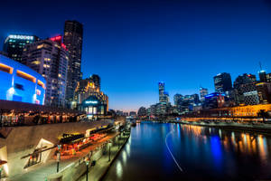 黃昏時分的城市天際線，燈火通明的建築物和河流倒影。