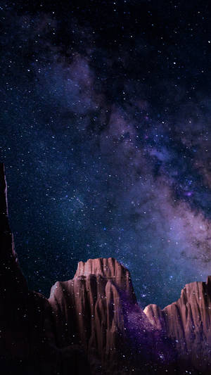 在繁星點點的紫色夜空下，崎嶇的岩石地貌與可見的星系。