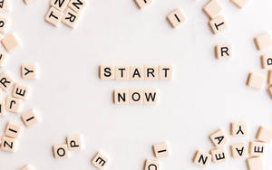 散落的字母瓷磚在白色表面上形成 'START NOW' 這個短語。