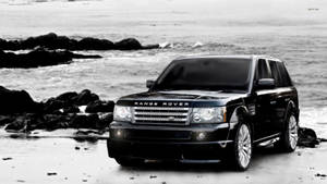 黑色Range Rover SUV停泊在岩石海灘上，海浪拍打。