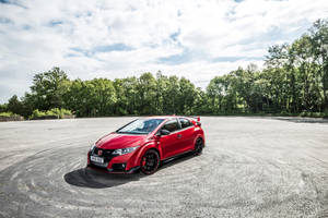 紅色本田 Civic Type R 停放在空曠的瀝青場地上，背景有樹木。