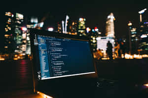 螢幕上顯示程式碼的筆記型電腦，以夜晚發光的城市為背景。 — MacBook Pro 壁紙