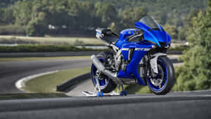 藍色Yamaha R1電單車停在賽道上，後面有綠色樹木。 — iMac 壁紙