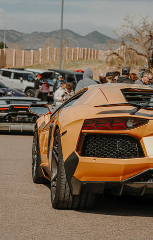 橙色林寶堅尼Aventador在車展上，背景有群眾和山脈。