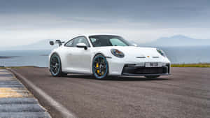 白色保時捷911 GT3 RS行駛於海岸公路，背景為大海和山脈。