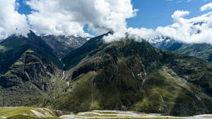 白雪覆蓋的山峰、翠綠山坡、藍天白雲。