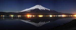 夜晚湖中倒映的富士山，岸邊燈光閃爍。 — 雙螢幕 壁紙