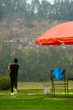 高爾夫球手在紅色雨傘下、草地上準備揮桿。