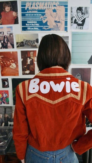 穿著紅色Bowie外套的人面向音樂海報牆。