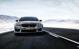 銀色BMW M5在日落時分於沙漠公路上奔馳，背景是雪山。
