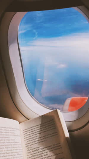 飛機座位上的打開書本，窗外雲朵和機翼景色 — 旅行 壁紙