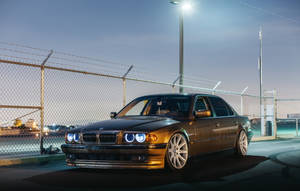 金色BMW房車在黃昏時停泊在街燈下的鐵絲網圍欄後面。