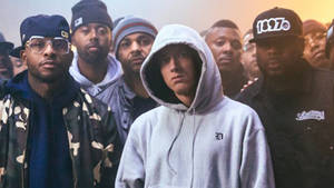 Eminem 身穿灰色連帽衫，在溫暖燈光下被穿著街頭服飾的男子包圍。