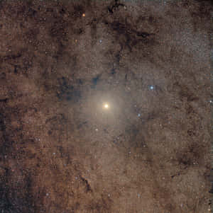 一個宇宙星雲，帶有黑暗塵埃帶和發光的恆星，圍繞著一顆明亮的黃色恆星。 — iPad (A16) 壁紙