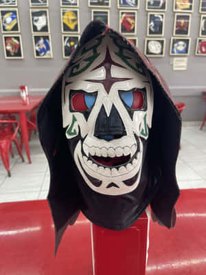 一個色彩繽紛的 lucha libre 面具，帶有骷髏設計，放在餐廳的紅色底座上。 — 鬼滅之刃面具 壁紙