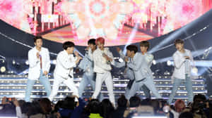 K-pop團體在舞台上表演，燈光明亮，前景有觀眾。