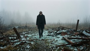 一個男人獨自走過一個充滿霧氣、佈滿碎玻璃和生鏽金屬的田野。