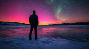 人站在雪地上觀看夜間冰凍湖泊上空多彩的北極光
