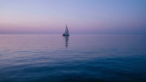 帆船在暮色中漂浮在平靜的水面上，帶有紫色和藍色色調。