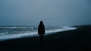 一個孤獨的人影站在黑暗的海灘上，面對著暴風雨天空下拍打的海浪。