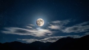 滿月在繁星點點的夜空和薄雲下，從山脈後升起。