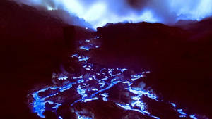 發光的藍色熔岩在夜間流經黑暗的火山地形。