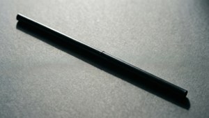 一支黑色筆斜放在灰色有紋理的表面上，帶有明顯的陰影。