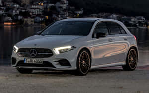 銀色 Mercedes-Benz A-Class 停泊在水邊，後面有亮燈的房屋。 — MacBook Air M1 壁紙