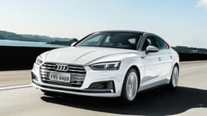 白色奧迪轎車在湖邊高速公路上行駛，背景有山丘。 — Audi R8 GIF 壁紙