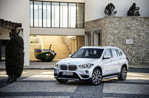 白色BMW SUV停泊在現代房屋前，房屋有石牆和玻璃窗。 — Surface Pro 壁紙